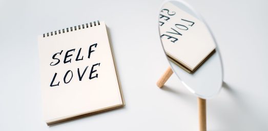 Self love, state of appreciation for oneself, physical, psychological and spiritual growth, taking care of own needs, wellbeing. Notepad with text Self love and reflection in the mirror.